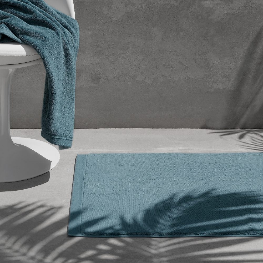 Teal bath mat on a grey floor with a matching towel over a white chair